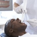 Paciente homem deitado na cadeira odontológica e dentista homem escaneando com um scanner intraoral a arcada dentária deste paciente.