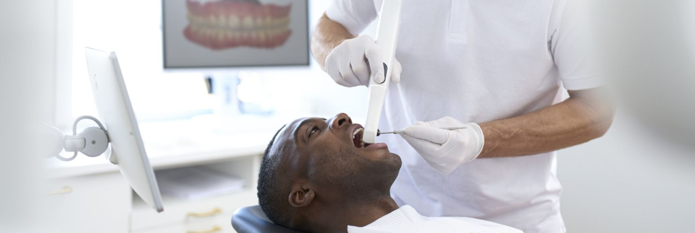 Paciente homem deitado na cadeira odontológica e dentista homem escaneando com um scanner intraoral a arcada dentária deste paciente.